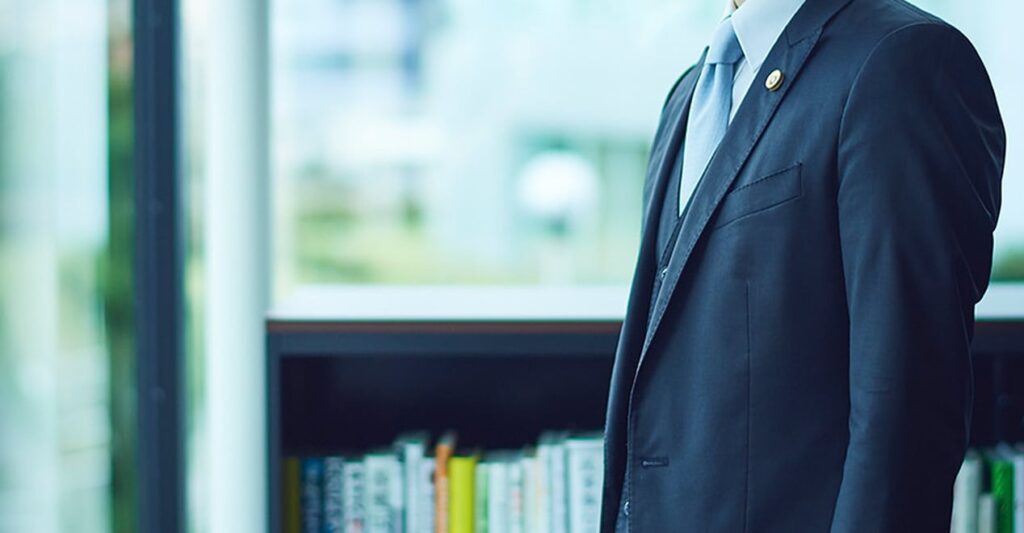 書棚の前に立つ、弁護士バッジを付けた弁護士