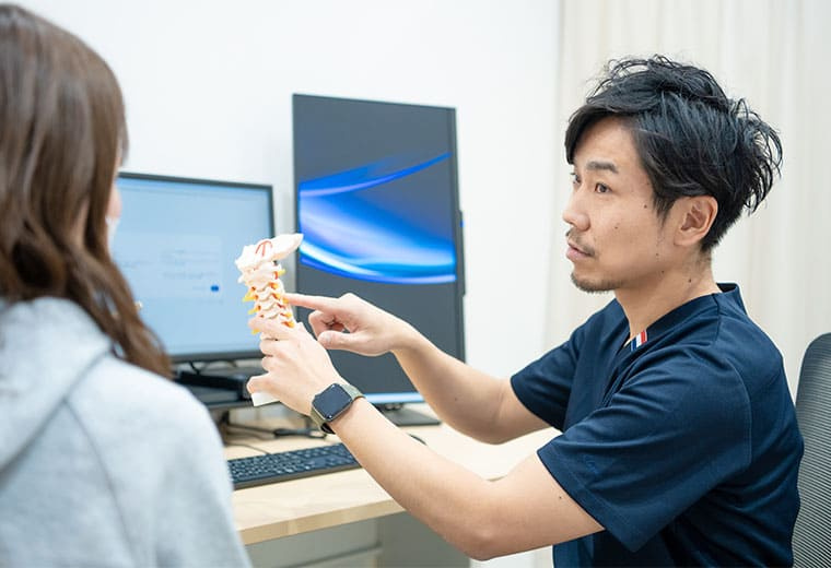 なかお三国ペインクリニックの中尾謙太院長が背骨の模型を使って患者さんに説明する様子