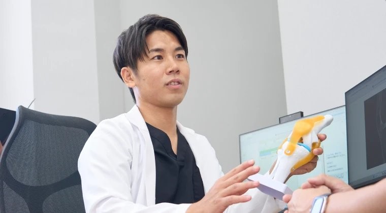 膝関節の模型を手に、治療の考え方を説明する宮路啓太院長